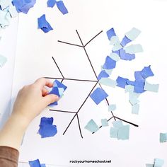 a child's hand is making a snowflake craft with blue and white paper