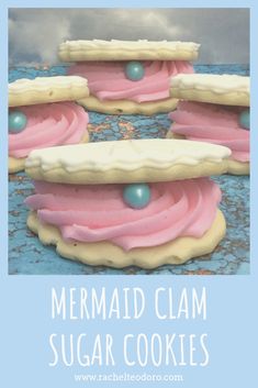 three cookies with pink icing and blue balls on them, sitting in front of the words mermaid clam sugar cookies