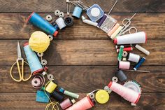 sewing supplies arranged in the shape of a circle on top of a wooden table with scissors, thread and spools