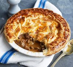 a pot pie with meat and gravy in a white dish on a blue napkin