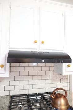 a tea kettle sitting on top of a stove next to white cupboards and cabinets