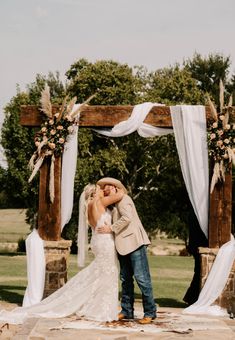 a bride and groom kissing under an outdoor wedding arch