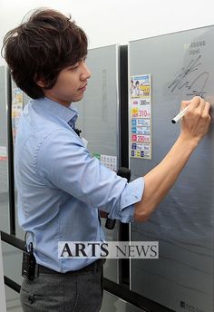 a man writing on the side of a refrigerator with magnets and papers attached to it