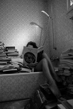 a woman sitting on the floor reading a book in front of a pile of books