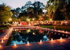 candles are lit in the middle of a pool surrounded by greenery and trees at night