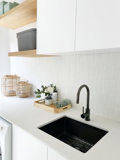 a kitchen with white cabinets, black sink and wooden shelf above the sink is a washer and dryer