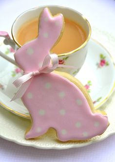 a pink bunny cookie sitting on top of a plate next to a cup of tea