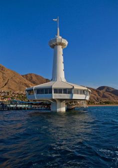 an unusual building in the middle of water with mountains in the backgrouds