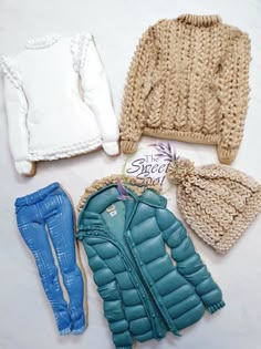 doll clothes and accessories are laid out on a white surface, including a sweater, jacket, leggings, and boots