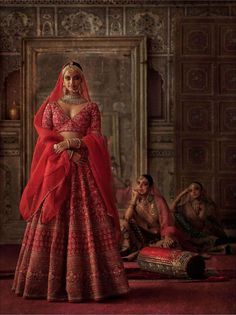 a woman in a red and gold wedding dress standing next to a man sitting down