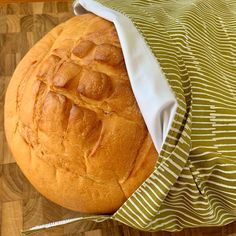 a loaf of bread is wrapped in a green and white striped cloth on a wooden table