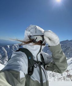 a person with long hair wearing a white jacket and hat on top of a snow covered mountain