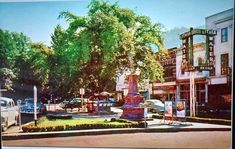 an old photo of a town square with cars parked on the street and trees in the background