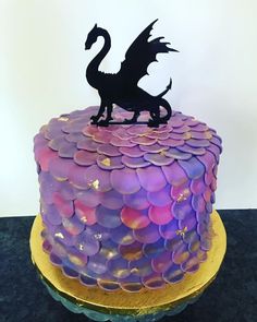 there is a cake that looks like a dragon on top of the cake with purple and pink icing