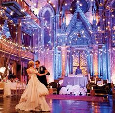 a bride and groom dance together in an ornate ballroom with fairy lights strung from the ceiling