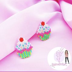 a pair of colorful cupcake earrings sitting on top of a pink cloth