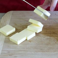 a person cutting cheese with a knife on a wooden board and chopping it into cubes