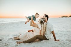 a man, woman and baby are sitting on the sand at the beach with an orange sky in the background