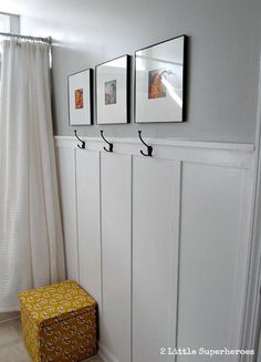 a white bathroom with three pictures hanging on the wall and a yellow stool in front of it