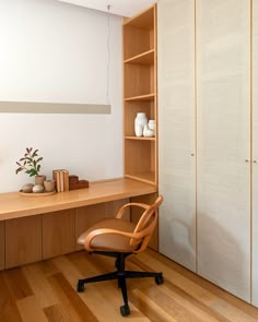 an office chair sits in front of a wooden desk and bookcase with vases on it