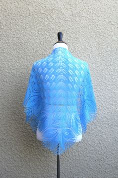 a mannequin wearing a blue shawl on top of a white table next to a wall