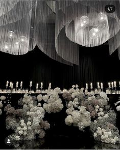 a chandelier with flowers and candles hanging from it's sides in front of a black background