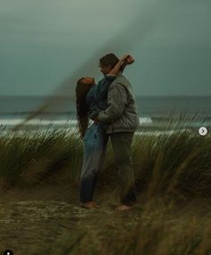 a man holding a woman on his back while standing in the grass by the beach