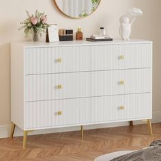 a white dresser with gold handles and drawers in front of a round mirror on the wall