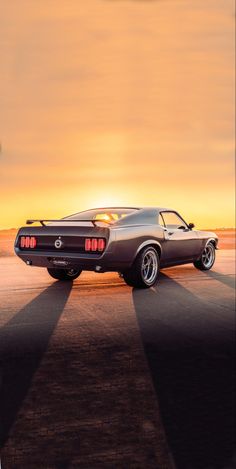 an old muscle car parked on the side of the road in front of a sunset