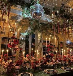 a dining room decorated with candles, plates and flowers in front of a mirror ball hanging from the ceiling