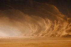 a large group of clouds are in the sky over a desert area with people walking on it