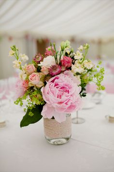 a vase filled with pink and white flowers sitting on top of a table covered in tables cloths