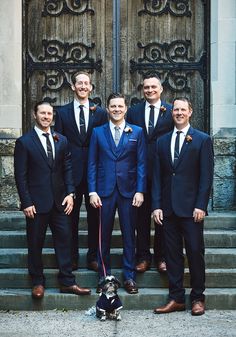 a group of men standing next to each other in front of a door with a dog on a leash