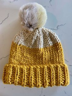 a yellow and white knitted hat with a pom - pom on top