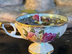 a teacup with flowers on it and a lit candle in the middle is sitting on a table