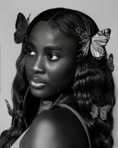 a black and white photo of a woman with butterflies on her head, looking at the camera