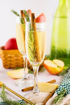 two wine glasses filled with champagne and garnished with cinnamon sticks, rosemary sprigs, and apple slices