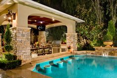 an outdoor kitchen and pool area with stone pillars around the pool, covered in lights