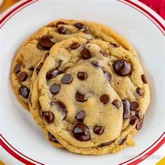 three chocolate chip cookies on a white and red plate with a yellow striped towel in the background