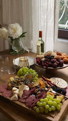 a wooden table topped with lots of different types of cheeses and crackers next to a bottle of wine