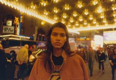 a woman standing in the middle of a crowded street at night with lights hanging overhead