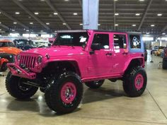 a pink jeep is parked in a showroom with other cars and trucks behind it