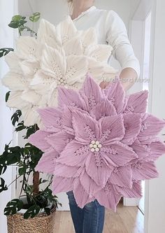 a woman standing in front of a potted plant and holding two large white flowers