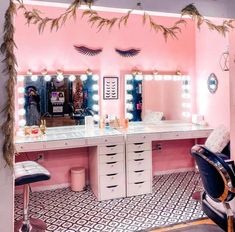 a room with pink walls and lights on the vanity area, including an upholstered chair