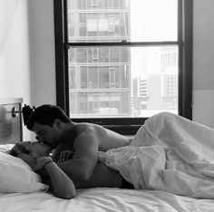 a man and woman laying in bed with the sheets pulled back to each other as they kiss