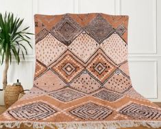 an orange and brown blanket sitting on top of a wooden floor next to a potted plant