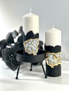 two black and white candles sitting next to each other on top of a stand with rocks