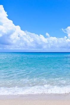 an empty beach with blue water and white clouds