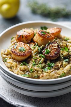 a white bowl filled with rice and scallops on top of a table next to lemons