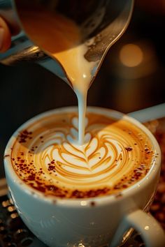 someone pours milk into a cup of cappuccino in a saucer